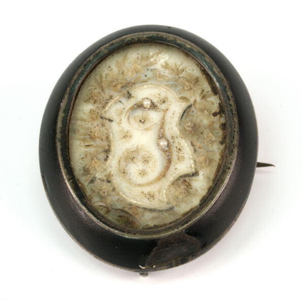 Rouwbroche met haarwerk 'J' in zilveren zetting met zwarte rand, medaillon met foto op achterkant