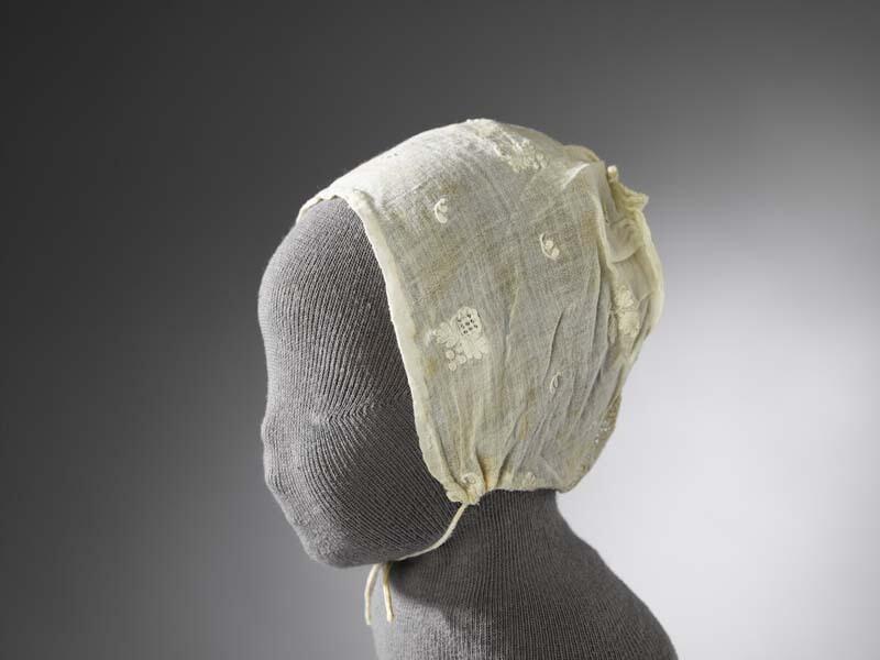 Kindermutsje van neteldoek, tulen inzetstukje aan de achterkant, met wit opgelegde bloemetjes