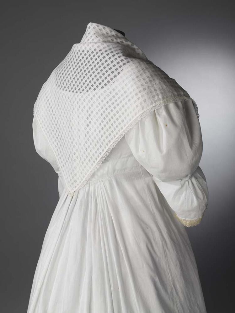 Driekantig omslagdoekje (fichu) van wit neteldoek met hokjespatroon en langs de zijden een smal…