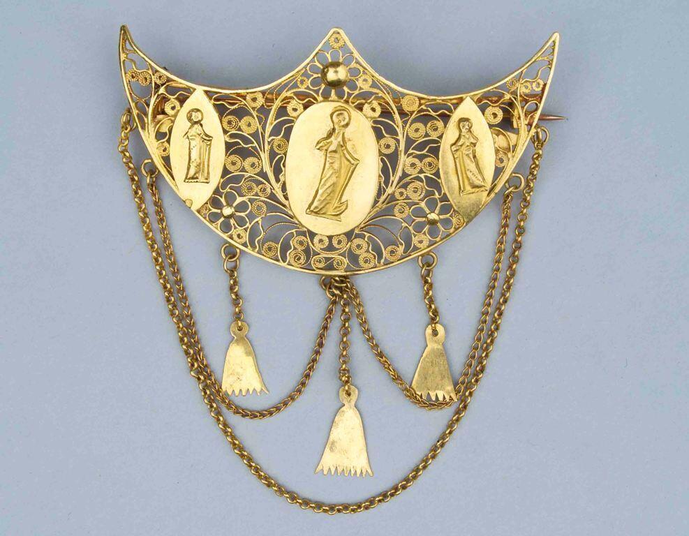 Broche van filigrain goud waarop drie plaatjes met menselijke figuren en onderaan hangen kettinkjes…