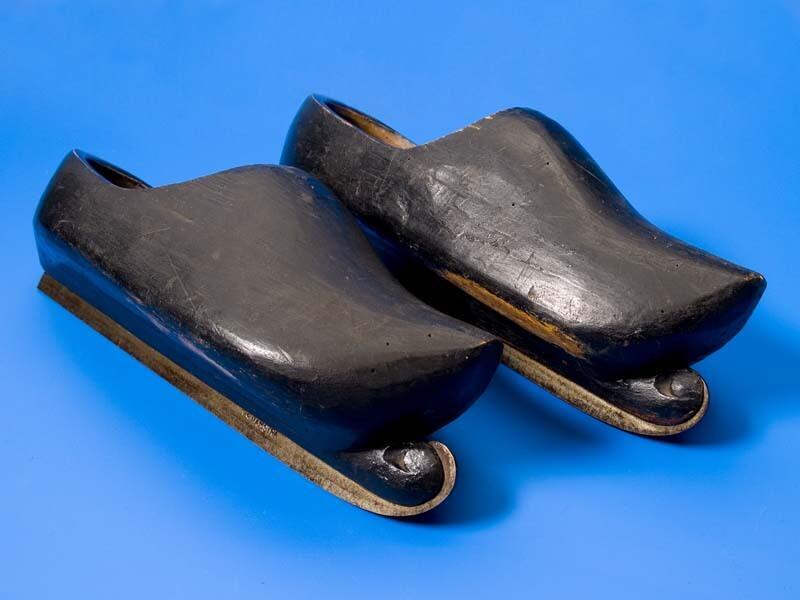 Paar klompschaatsen, zwart geverfde houten klompen waarbij onder de zool een schaatsijzer is…