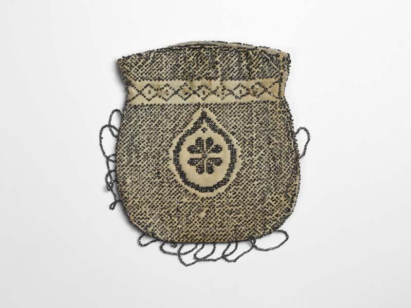 Wit katoenen tasje met zwart-zilverkleurige opgenaaide kraaltjes, in het midden een bloem in een…