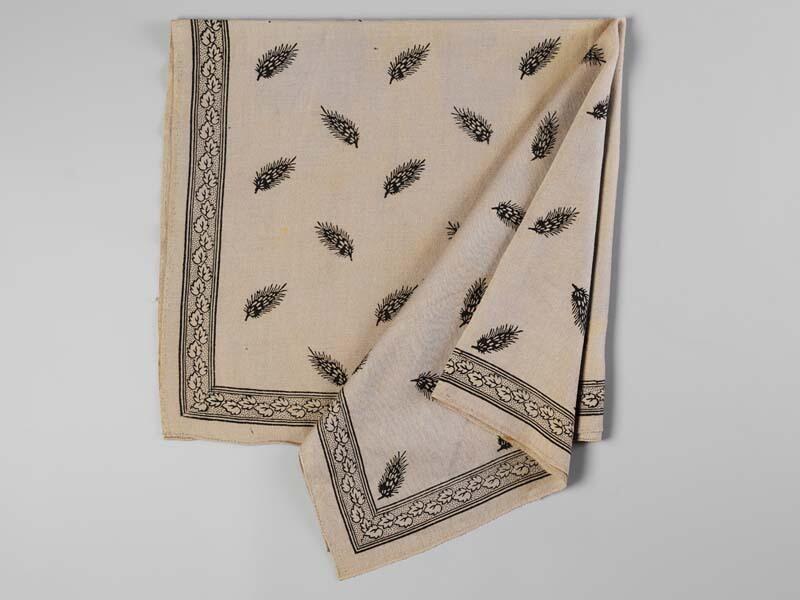 Vierkante wollen doek in beige kleur, bedrukt met zwarte veervormige blaadjes, langs de zijden een…
