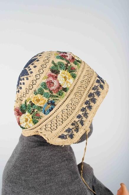 Gebreid mutsje van wit katoen met ster en bloemmotieven van veelkleurige kralen