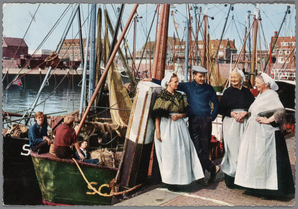 Man en drie vrouwen in Scheveningse streekdracht aan de haven, voor 1970