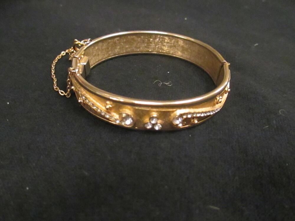 Armband, type 'bangle', van verguld metaal met opstaand ornament bezet met witte strass-stenen