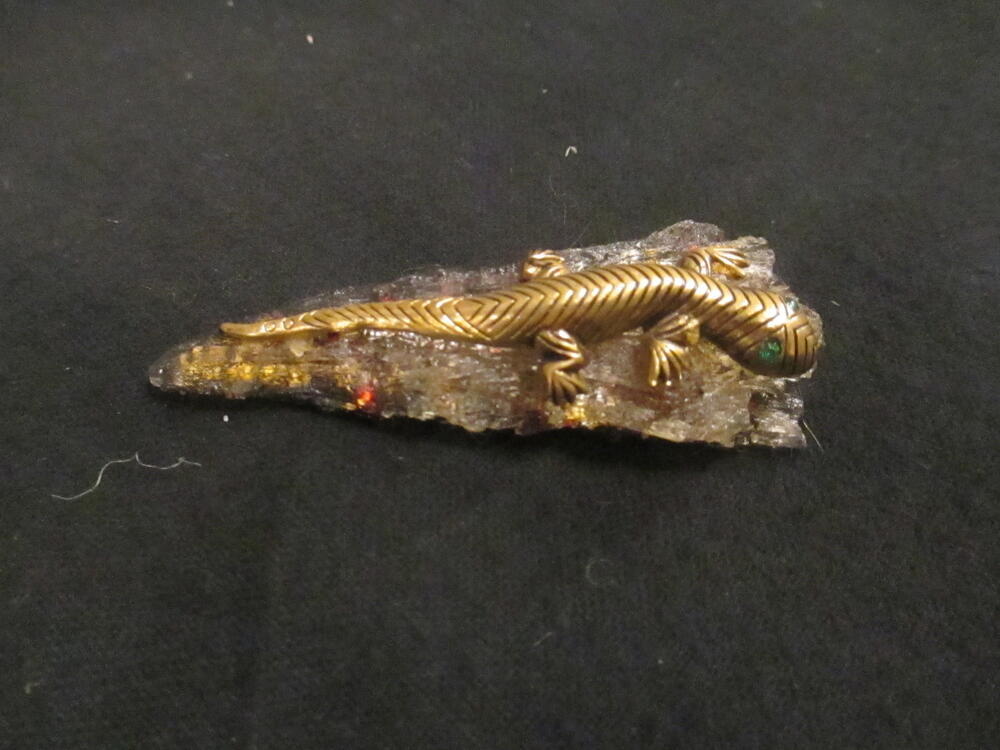 Broche van grijs kunsthars met metallic confetti, waarop goudkleurige metalen gekko