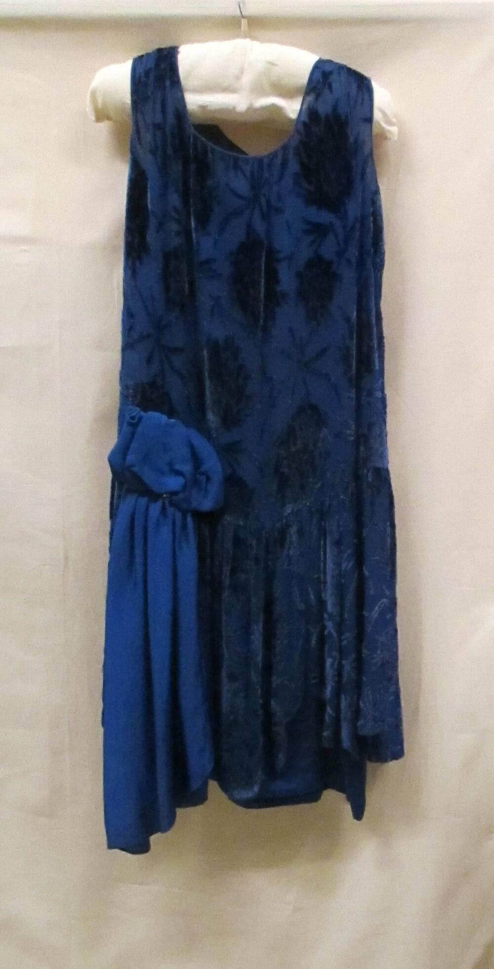 Avondjurkvan blauwe crepezijde, met bloemmotief in blauw in Ausbrennertechniek, blauwe strik rechts…