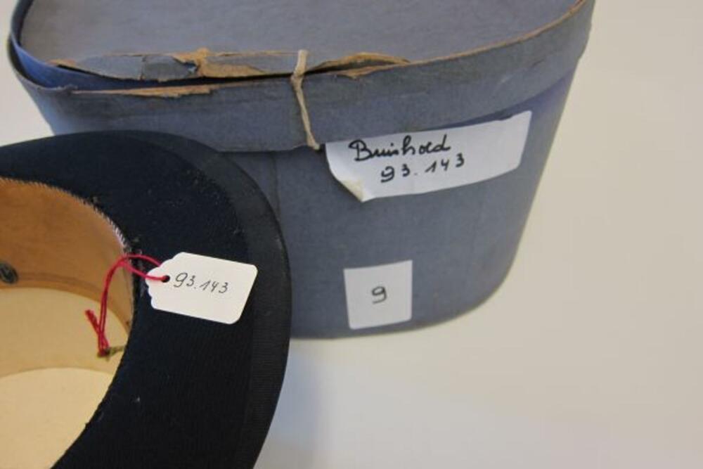 Ensemble bestaande uit een zwarte buishoed in originele grijze hoedendoos.