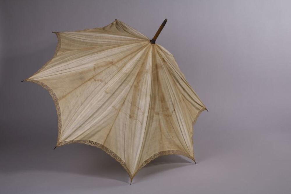 Ecrukleurige parasol met rand van filetkant en houten steel met leren draaglint