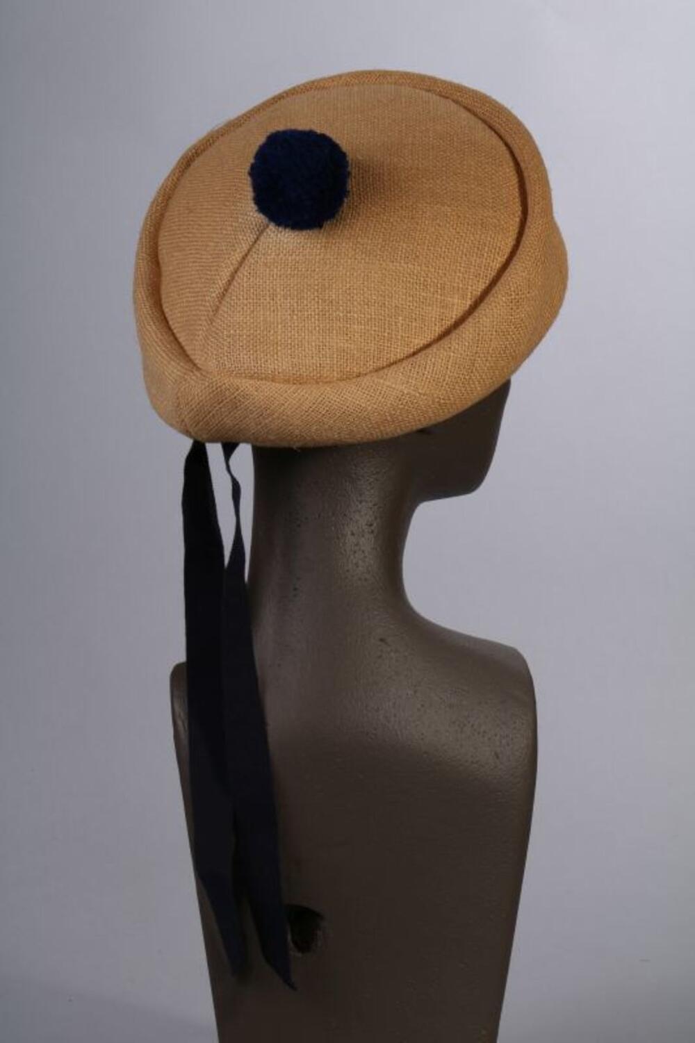 Hoed in beige jute met donkerblauwe pompon en geribde linten
