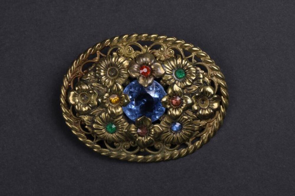Broche in metaal met versiering van groene, blauwe, oranje en rode stenen