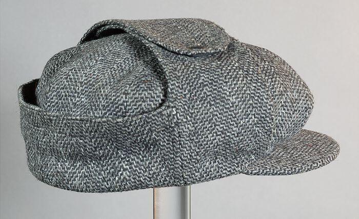Ronde grijze winterpet, met aan de zijkanten twee flappen die bovenop met twee drukkers vastgezet…