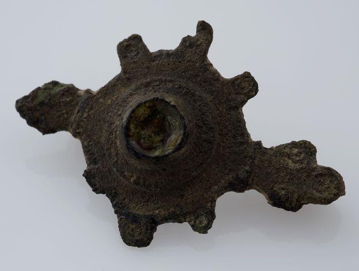 Bronzen fibula of mantelspeld in de vorm van getande cirkel met kleine email knop