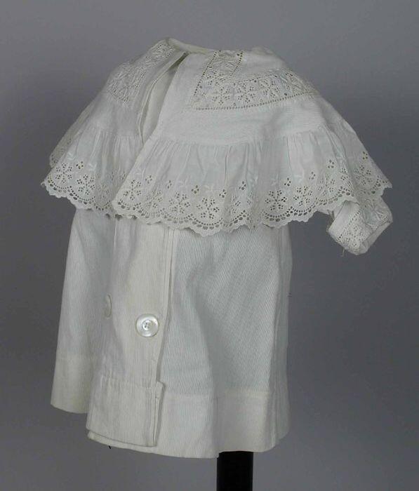 Kinderjas van wit ribspiqué met brede pelerinekraag, double breasted, broderie tussenzetsel in de…