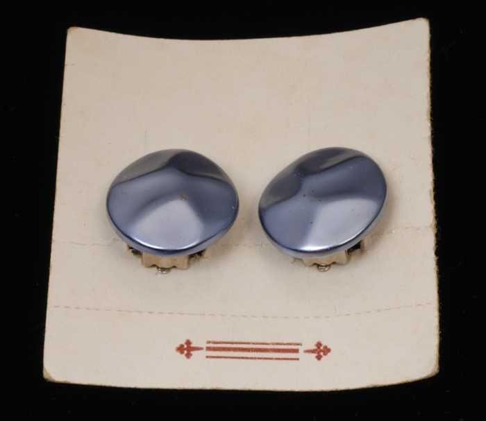 Paar oorbellen, clip met platte ovale gedeukte knop van blauw plastic met paarlemoerglans, op wit…
