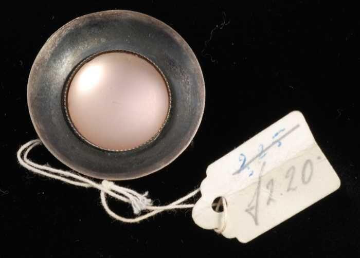 Broche van donker metaal, schotelvormig met een matte roze bolle 'steen' in het midden, kapper Van…
