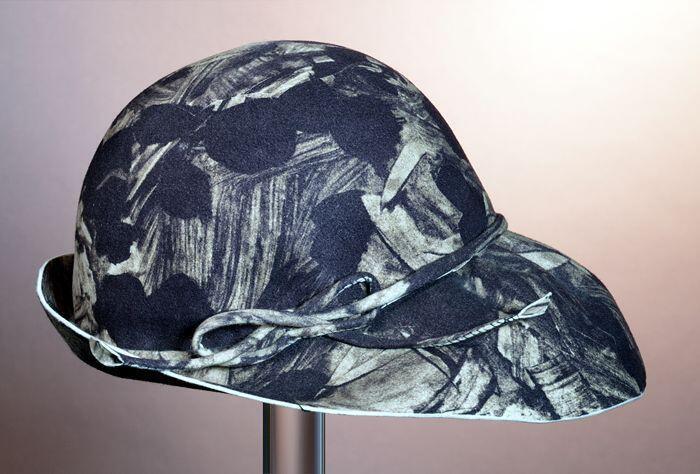 Cloche van cremekleurig vilt bedrukt met print in zwart, rand achter smal, voor breed uitlopend,…
