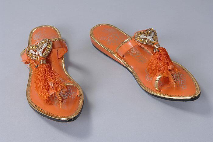 Oranje imitatie-lakleren teenslippers met teenband, kwastjes, goudkleurige details, kralen en…