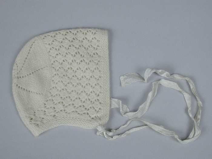 Babymuts gebreid van crèmekleurige dunne wol in tricotsteken en ajour, stervorm op de bol, satijnen…