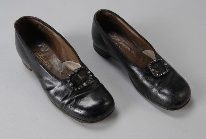Zwarte leren kinderschoenen met bolle neus, op de voorvoet een siergesp met strass-steentjes, lage…