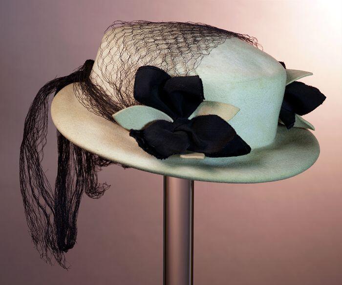 Crèmekleurige dameshoed van vilt met donkerblauw voile, deels over de bol, garnering van twee…