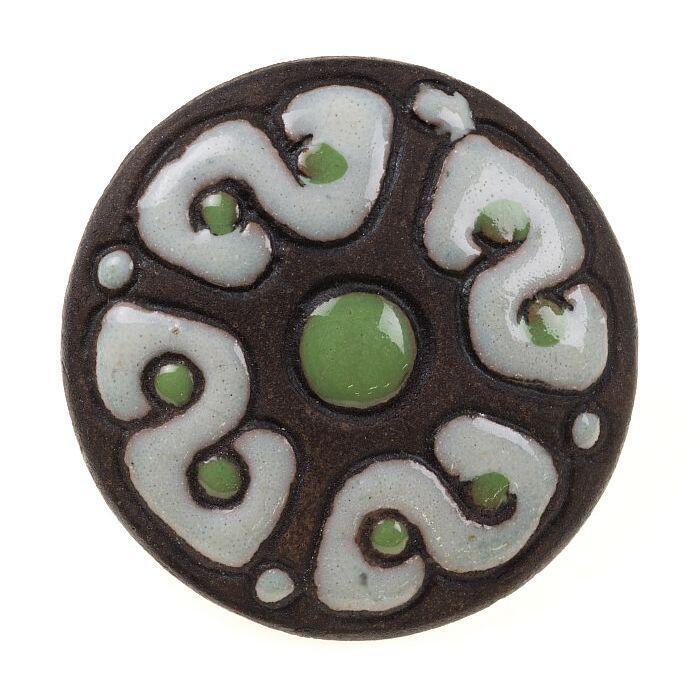 Ronde broche van gebakken klei, deels voorzien van wit en groen glazuur