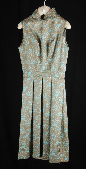 Knielange mouwloze japon van glanzende beige stof met turquoise dessin, met diep uitgesneden rug,…