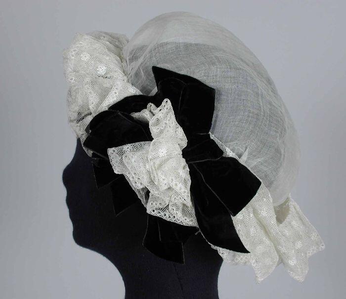Boudoirmuts van wit batist, kantruche over de bol, dubbele kantruches rondom, zwart fluwelen…