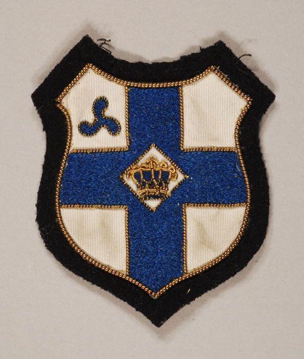 Stoffen badge, op zwart vilten achtergrond blauw kruis op wit fond met kroon en in…