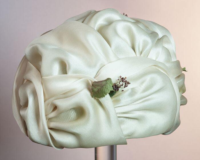 Hoed van gedrapeerd transparant beige satijn met vier corsages, blad en takjes