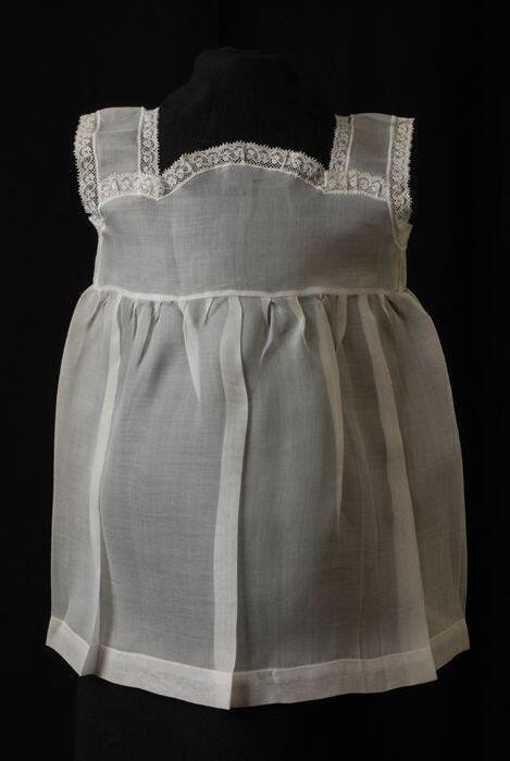 Babyjurk, mouwloos schortmodel van transparant wit nylonmet witte kantjes, 'Femifra' model 'Mona'