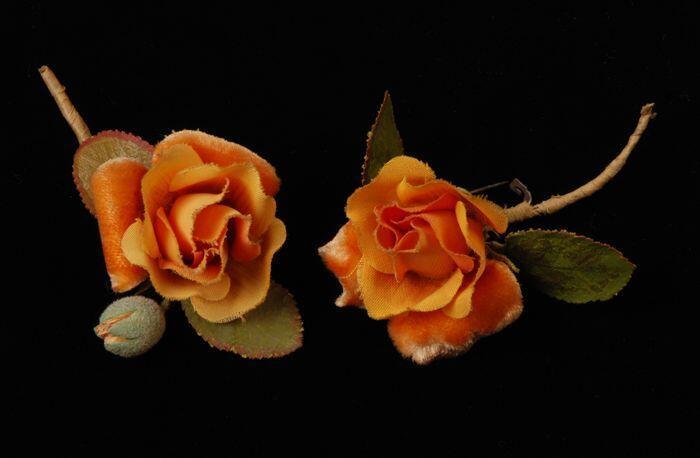 Twee corsages, kort groen steeltje met twee groen katoenen blaadjes, één geel oranje roos van…