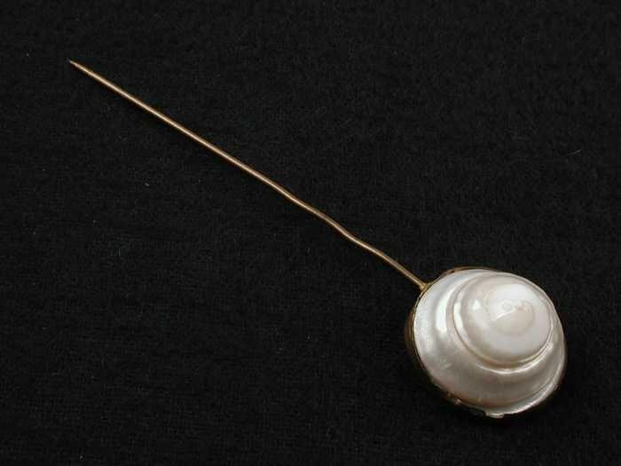 Hoedenspeld van gedraaide paarlemoeren schelp in koperen vattin met pin