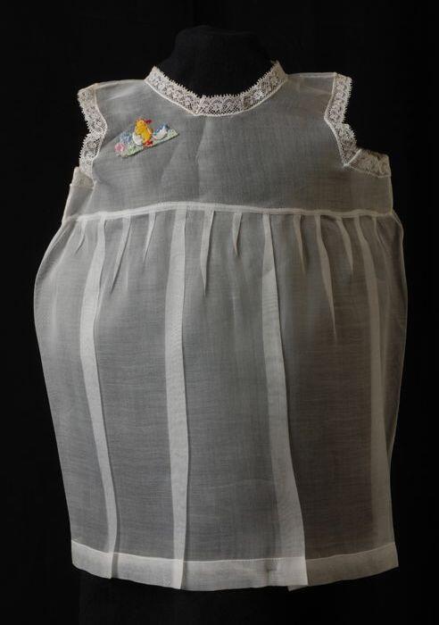 Babyjurk, mouwloos schortmodel van transparant wit nylonmet geborduurd kuiken en ei, 'Femifra'…