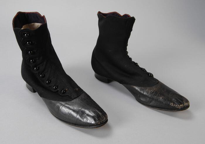 Zwarte bottins van keperstof met leren voorvoet en zijsluiting met knoopjes, bovenaan de schacht…