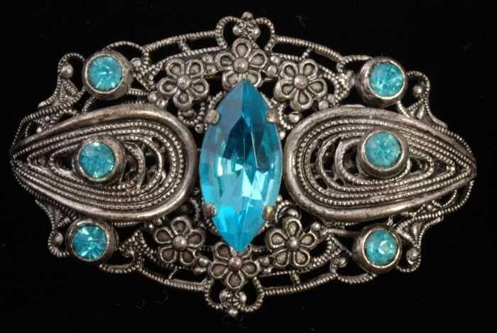 Broche, ornament van zilverkleurig filigrein metaal met lichtblauwe kunstdiamantjes, kapper Van…