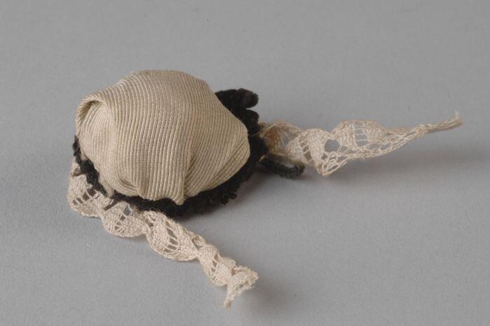 Mini hoed uit rechterdeel kastenwand, bonnet wit ribsatijn met zwarte band en pluk haar
