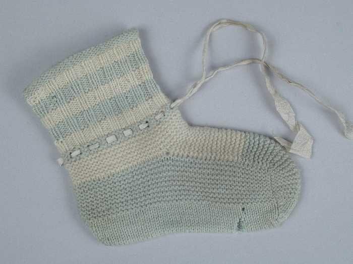 Paar babysokken gebreid van grijsblauwe en witte wol in tricot- en ribbelsteek, wit zijdelint door…