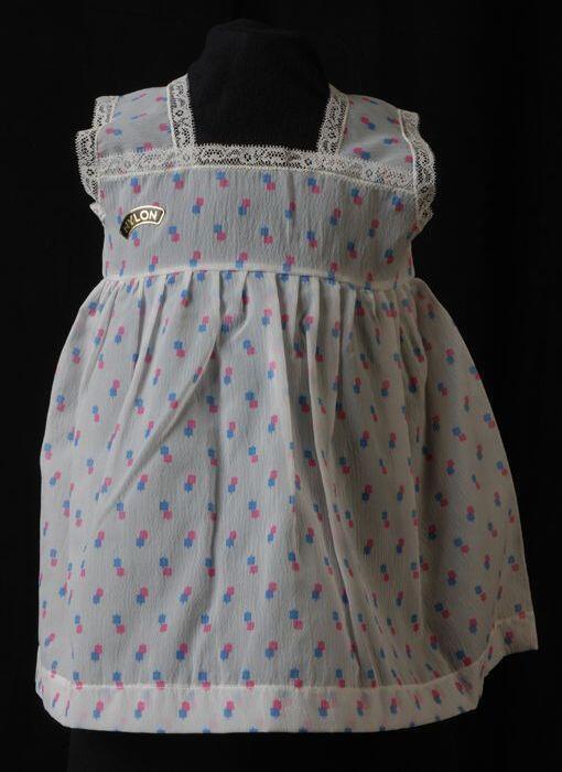 Babyjurk, mouwloos schortmodel van transparant nylonmet blauwe en roze blokjes, 'Femifra'