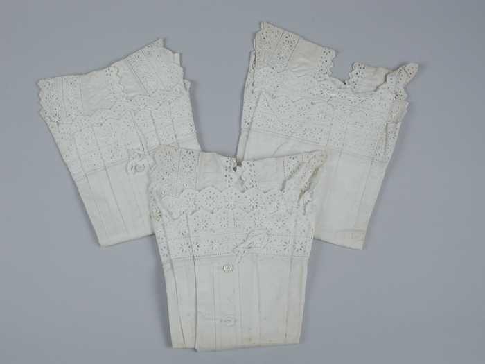 Drie identieke onderlijfjes van wit katoen met broderie langs hals en armsgaten, platte plooien en…