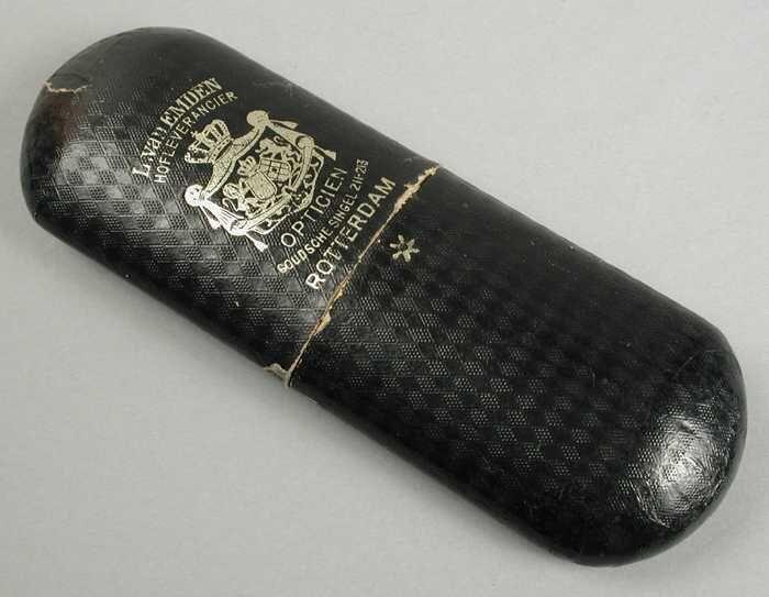 Brillenkoker van karton beplakt met zwart reliëf papier, twee in elkaar schuivende delen, "L. Van…