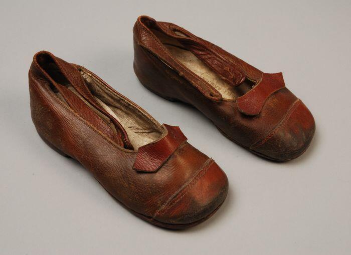 Bruine leren kinderschoenen met enkelbandje en neus en strik van rood leer, leren zolen