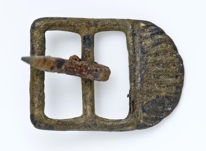 Kleine metalen gesp, rechthoekig en aan één zijdeversierd met halfronde schelpvorm