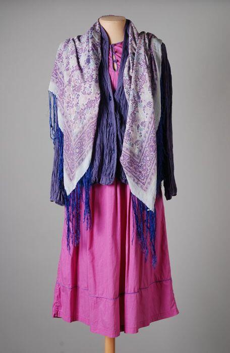 Mouwloze fuchsia overgooier, paarse blouse en sjaal met bloemmotief en rondom paarse franje