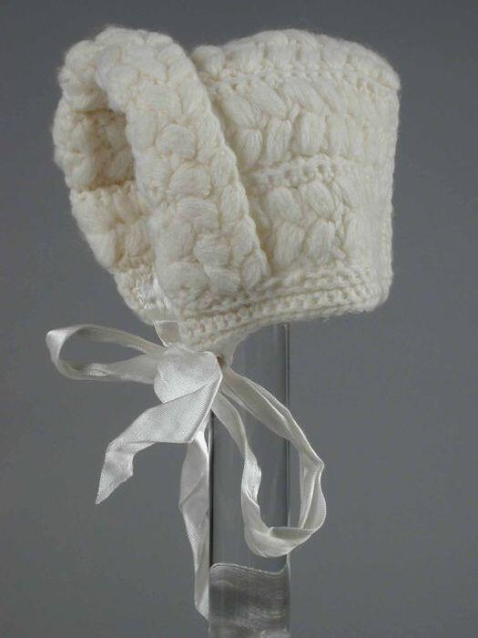 Babymuts gebreid van crèmekleurige wol in reliëfsteek met dikke noppen, wit satijnen strik bij de…