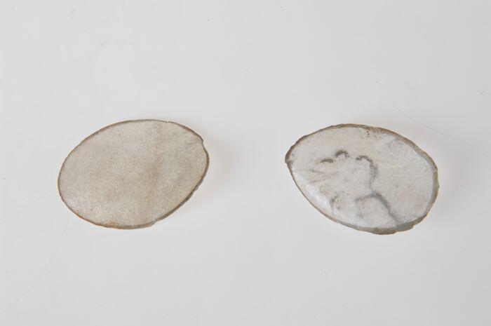 Twee losse brillenglazen, vervormd en dof, uit de brand van 14 mei 1940 afkomstig