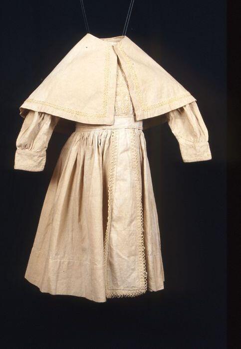 Kinderjurk met losse pelerine, ècrukleurig linnen met soutache, wijde rok, lange mouwen, lijfje met…
