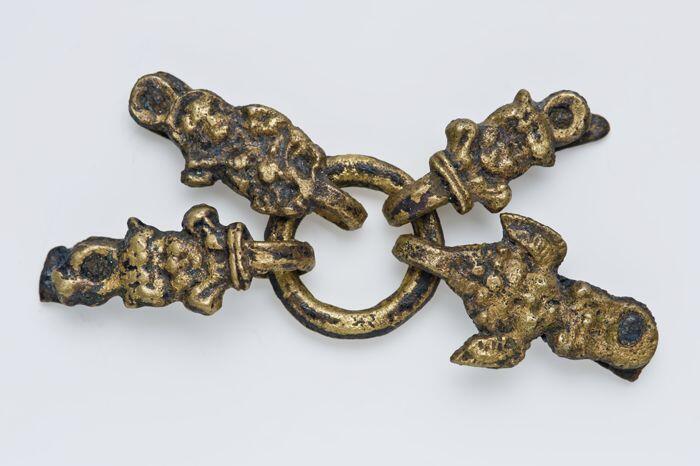 Metalen ring met vier riemtongen waarop in reliëf afbeelding van menselijke figuren
