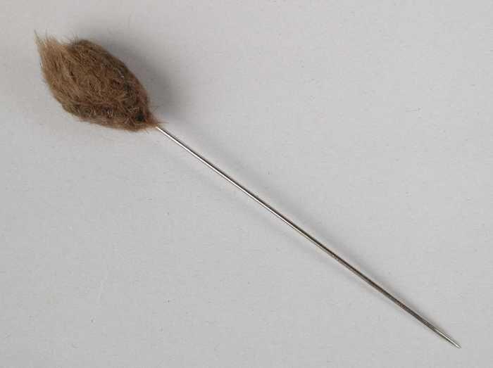 Hoedenspeld, korte metalen pin met scherpe punt, druppelvormige knop van bruin haarvilt (?)